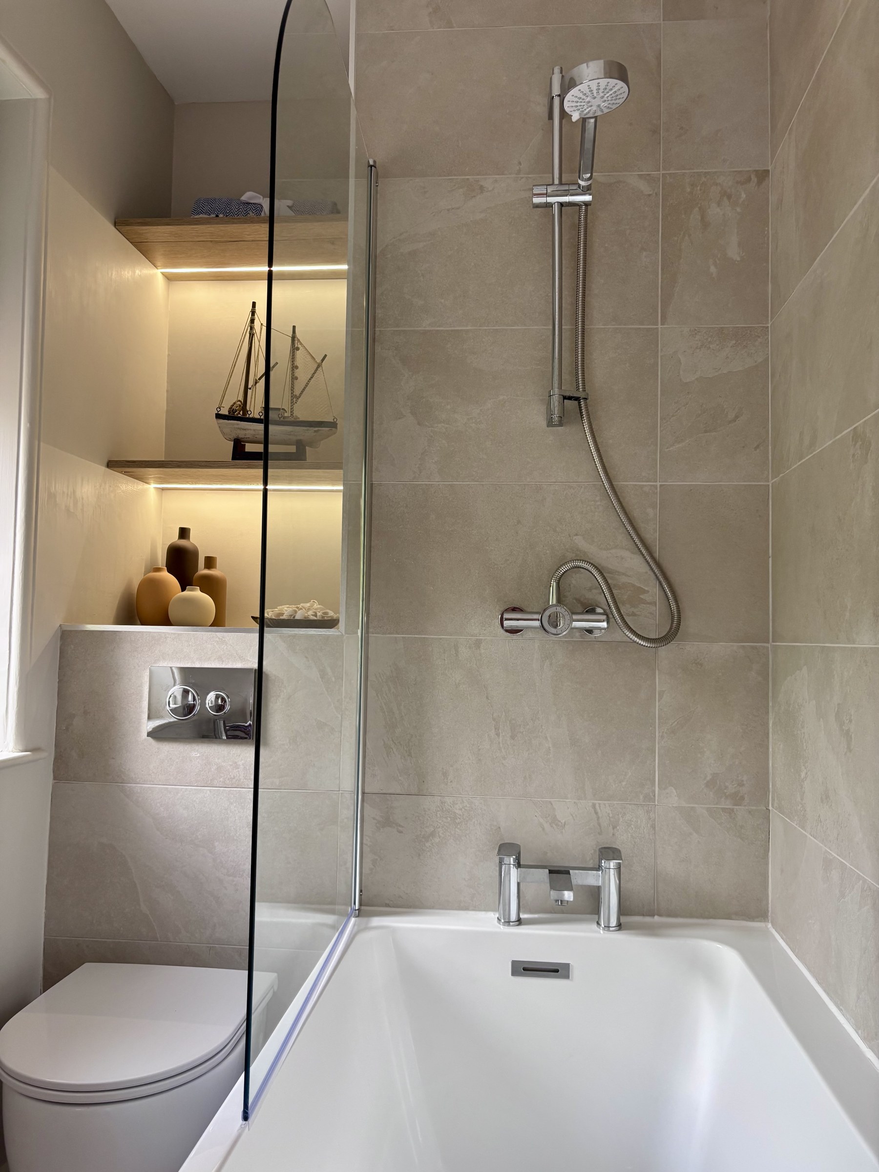 Bathroom with a bath, glass shower screen and illuminated shelving